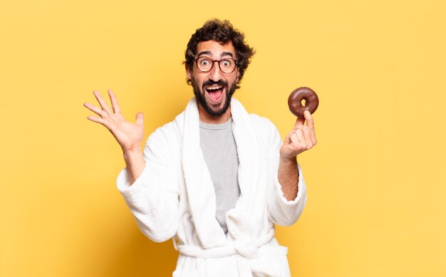 Young bearded man wearing bathrobe with a chocolate donut