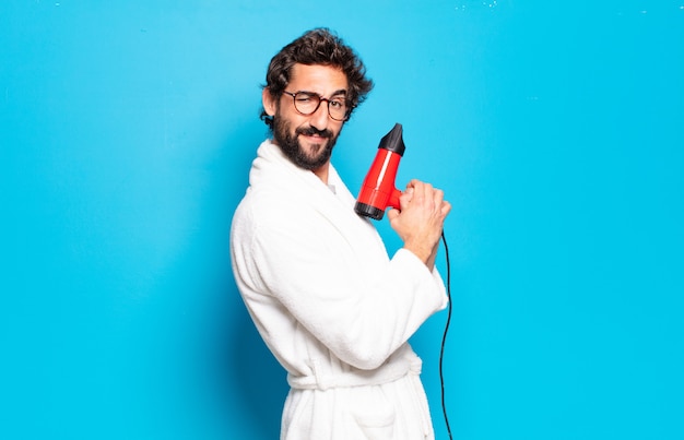 Young bearded man wearing bathrobe with a hairdryer