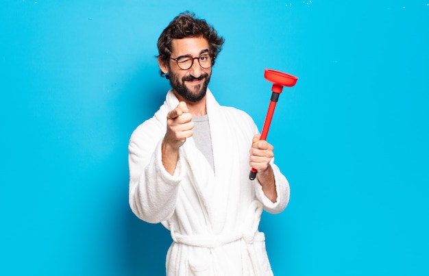 Young bearded man wearing bathrobe with a plunger