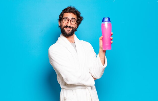 Young bearded man wearing bathrobe with shampoo and beauty products