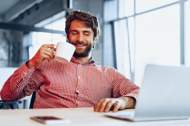 Young bearded man wearing casual shirt using his laptop computer. Businessman portrait