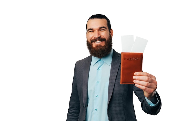 Young bearded man wearing jacket is holding his passport and two tickets