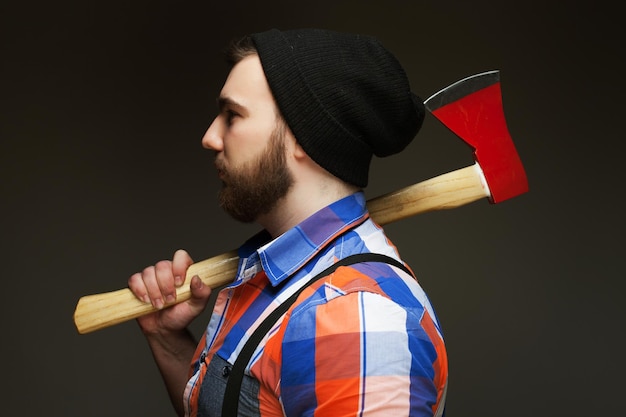 Young bearded man with big axe on shoulder standing against dark background