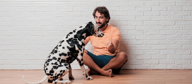 Young bearded man with a dalmatian dog against white brick wall 