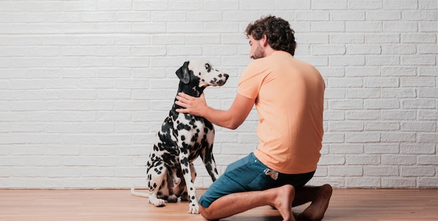 Photo young bearded man with a dalmatian dog against white brick wall