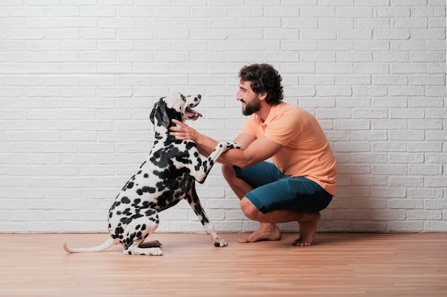 Young bearded man with a dalmatian dog against white brick wall 