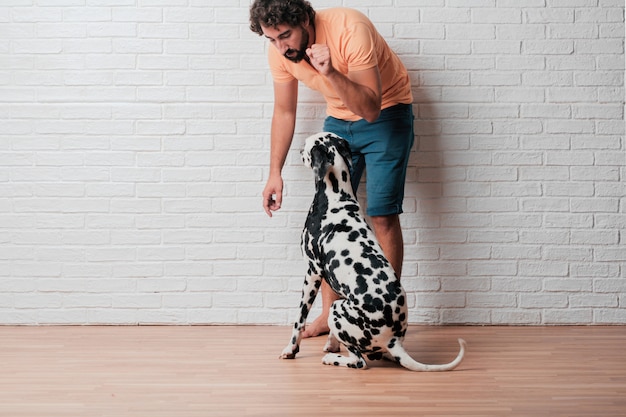 Young bearded man with a dalmatian dog against white brick wall 