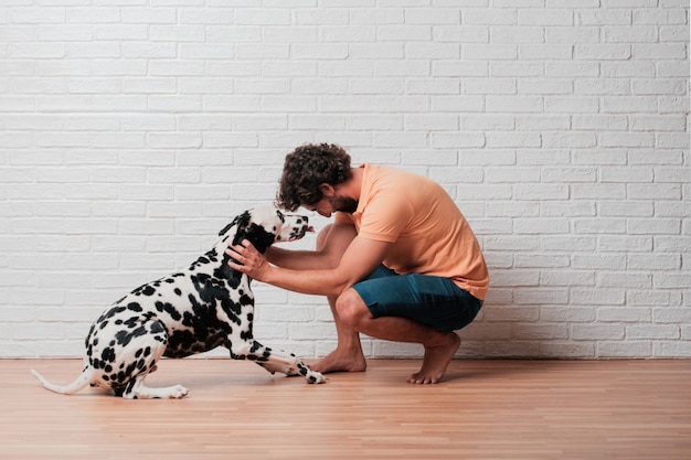 Young bearded man with a dalmatian dog against white brick wall 