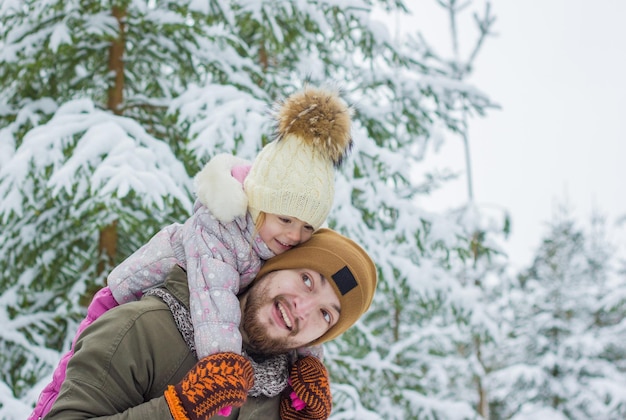 小さな女の子と若いひげを生やした男は冬の雪の森で楽しんでいます