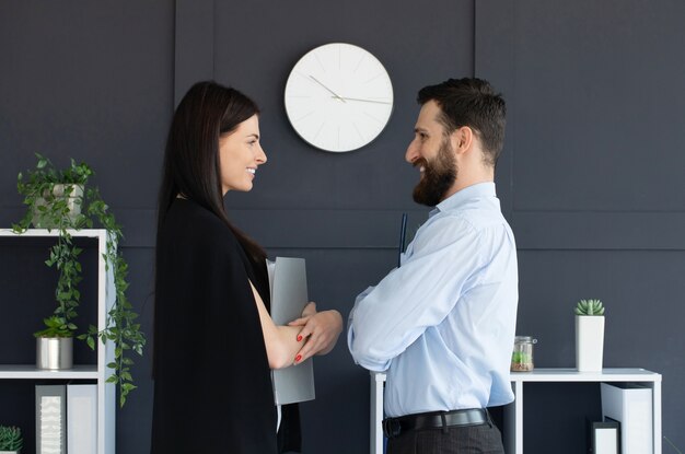 Young bearded man and woman in formalwear discussing something while holding folder with documents