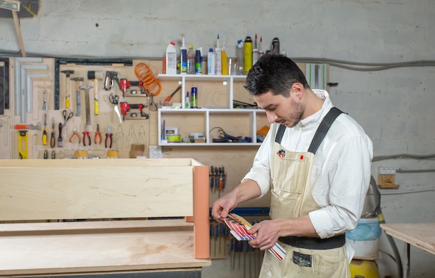 Молодой бородатый мужчина работает на мебельной фабрике, подбирает мебель по цвету.