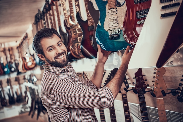 Giovane musicista barbuto compra la chitarra elettrica nel negozio di musica