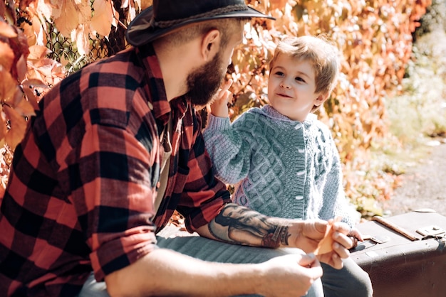 Young bearded tattooed hipster dad talks with his smiling little son father and son relaxing on a be...