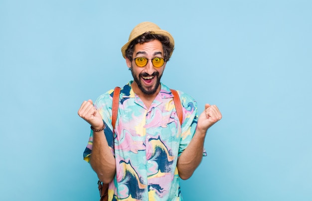 Young bearded tourist man feeling shocked, excited and happy, laughing and celebrating success, saying wow!