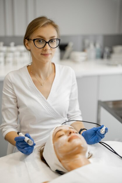 Young beautician doing microcurrent therapy on face