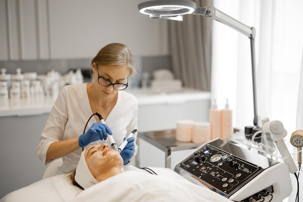 Photo young beautician doing microcurrent therapy on face