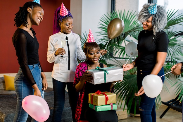 風船と帽子を持つ若い美しいアフリカ系アメリカ人の女の子は誕生日を祝い、誕生日プレゼントを贈ります。