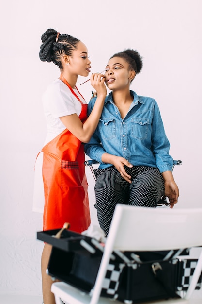 Young beautiful African American woman applying professional make-up by African make-up artist. Studio shoot