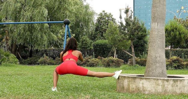 Young beautiful African American woman doing warming up and stretching with her leg in park.