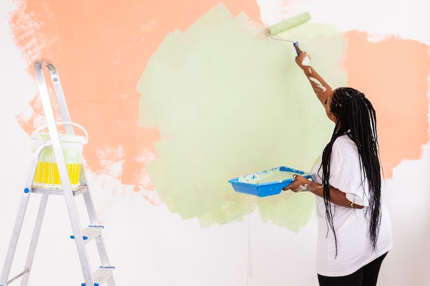 Young beautiful African American woman painting wall in her new apartment.