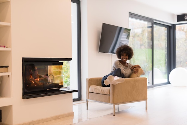 Young beautiful african american woman relaxing on chair in front of fireplace at autumn day