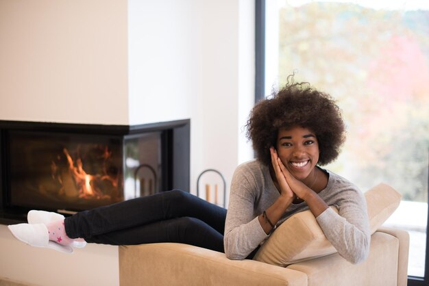 写真 秋の日に暖炉の前の椅子でリラックスした若い美しいアフリカ系アメリカ人女性