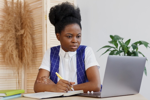 Молодая и красивая афроамериканка сидит за столом, смотрит в компьютер и делает заметки