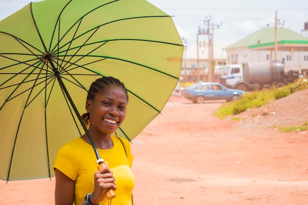 非常に晴れた天気の下で身を守るために傘を使用している若い美しいアフリカの女性
