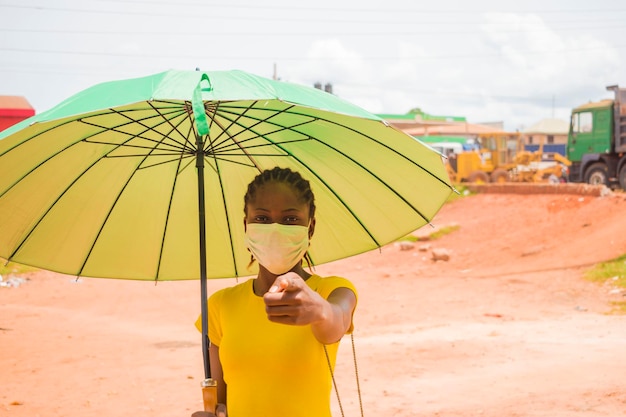 A young beautiful african lady wearing face mask prevent, preventing, prevented herself from the outbreak in the society and points at her face mask