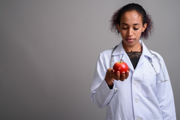 Young beautiful African woman doctor against gray wall