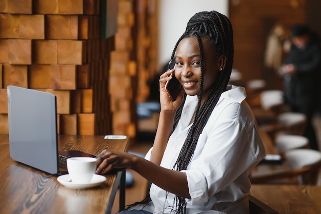 Young beautiful AfricanAmerican business woman talking on the phone while working in a cafe