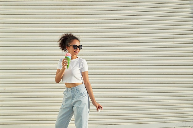 A young beautiful AfricanAmerican girl in a white tshirt and light jeans eats ice cream on a Sunny day selective focusing small focus area