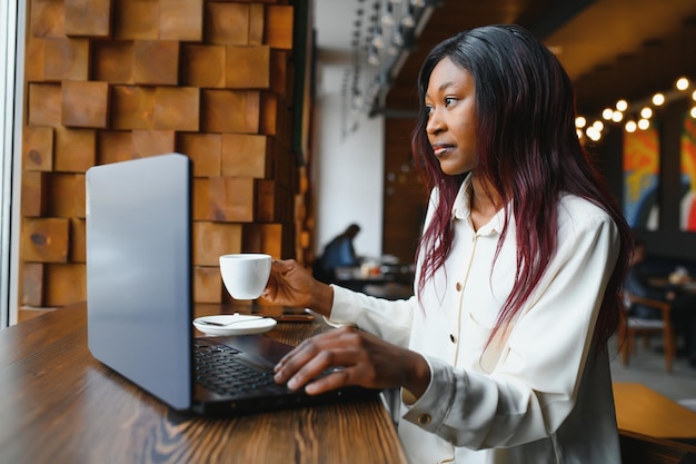 Young beautiful AfroAmerican businesswoman using laptop while working in cafe