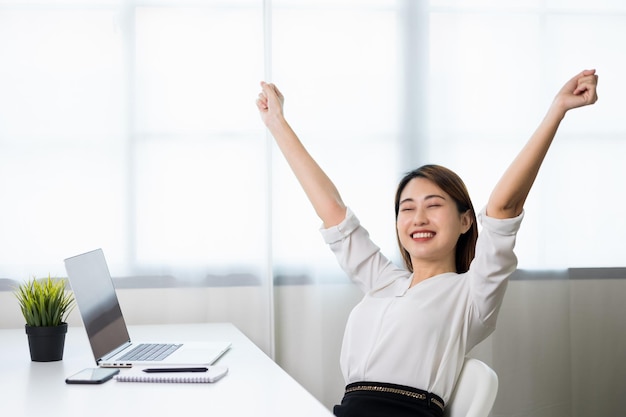 La giovane bella donna asiatica d'affari finisce di lavorare e festeggia con due mani allungate nell'aria. le donne hanno finito il lavoro e il riposo. lavora a casa in soggiorno.