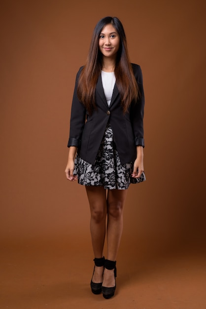 Young beautiful Asian businesswoman against brown background