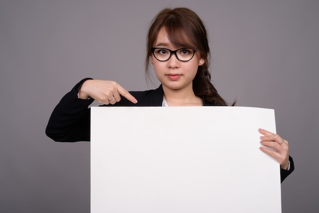 Young beautiful Asian businesswoman against gray wall