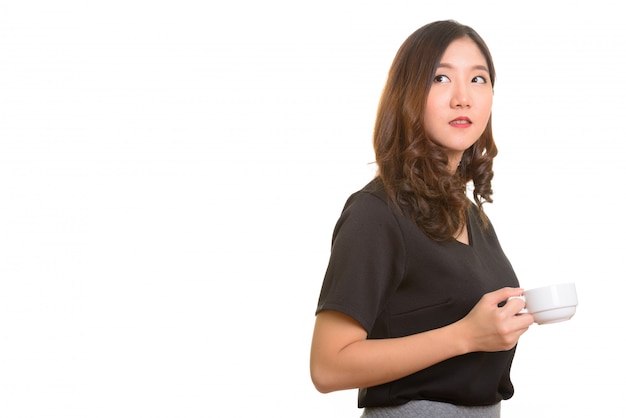 Молодая красивая азиатская деловая женщина держит чашку кофе во время мышления