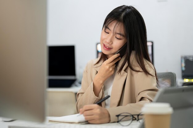 若い美しいアジアの実業家がオフィスで電話で話しながら仕事に忙しい