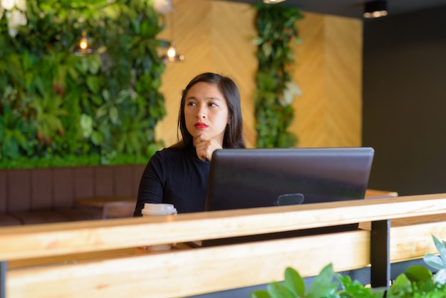 Young beautiful Asian businesswoman thinking with laptop at the coffee shop