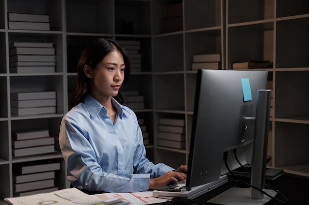 Young beautiful Asian businesswoman working with desktop computer in the office at night working overtime