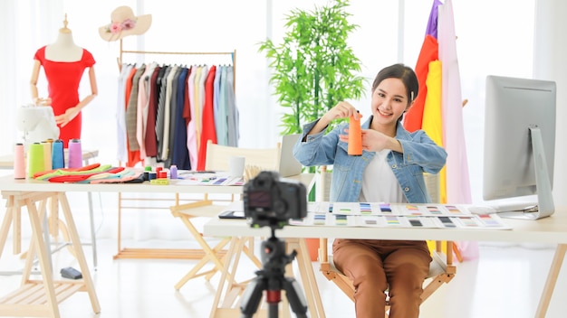 Young beautiful Asian fashion designers live video showing new material with consumer online network. She sales her product to people everywhere in the world. Blurred at foreground.