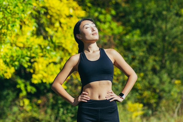 Молодая красивая азиатская спортсменка в черных леггинсах спортивного костюма и футболке отдыхает после тренировки с закрытыми глазами