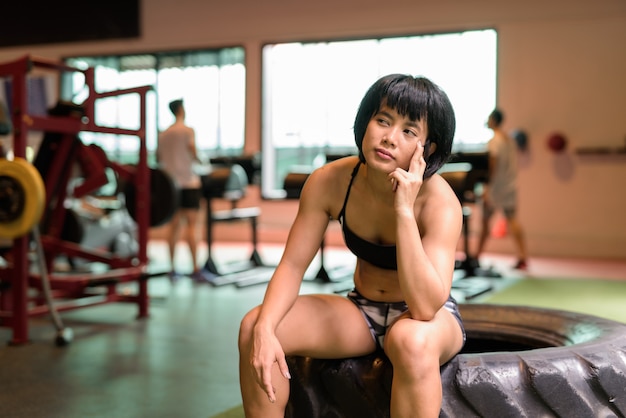 Молодая красивая азиатская фитнес-женщина, сидящая в тренажерном зале