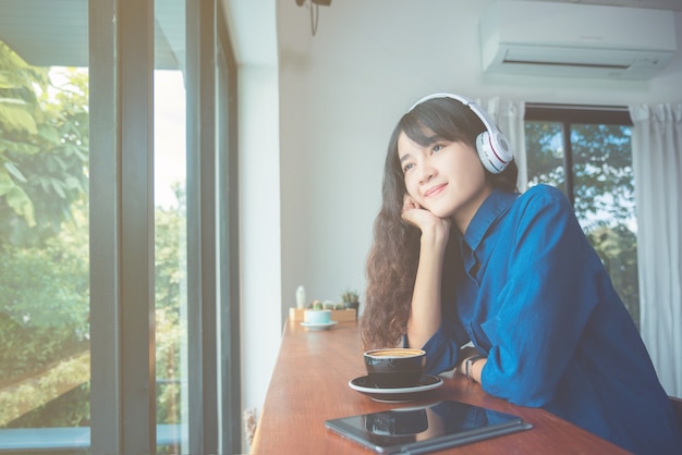 Young beautiful asian girl drinking coffee while listening music 