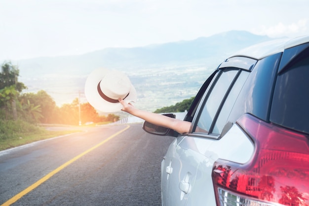 Photo young beautiful asian girl holding hat weave and reach out of the car at sunset