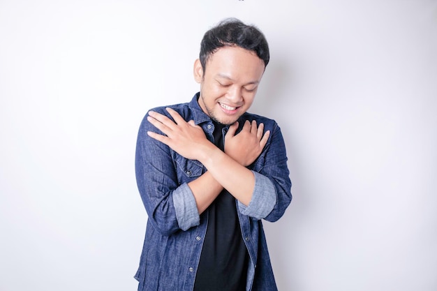 Young beautiful Asian man wearing casual navy blue shirt over white background hugging himself happy and positive smiling confident Self love and self care