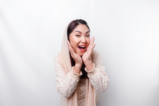 Young beautiful Asian Muslim woman wearing a headscarf shouting and screaming loud with a hand on her mouth communication concept