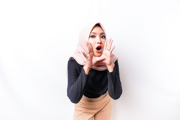 Young beautiful Asian Muslim woman wearing a hijab shouting and screaming loud with a hand on her mouth communication concept