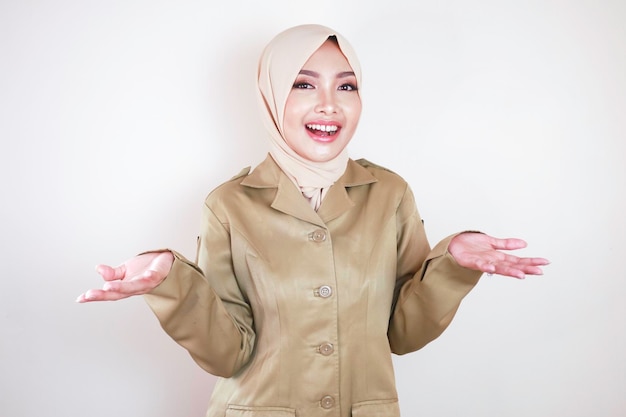 茶色のユニフォームとヒジャーブを身に着けている若い美しいアジアのイスラム教徒の労働者は、インドネシアのPNSを提示しています