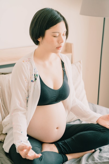 Young beautiful Asian pregnant woman meditating or doing yoga exercise at home. Relaxation yoga lotu